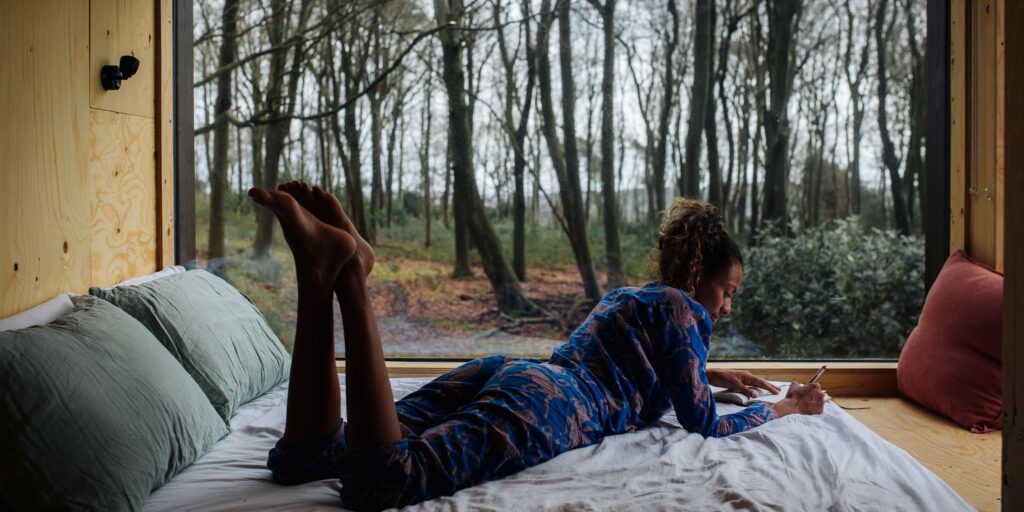 Woman writing in her journal while laying on a bed while staying in an Unplugged Cabin