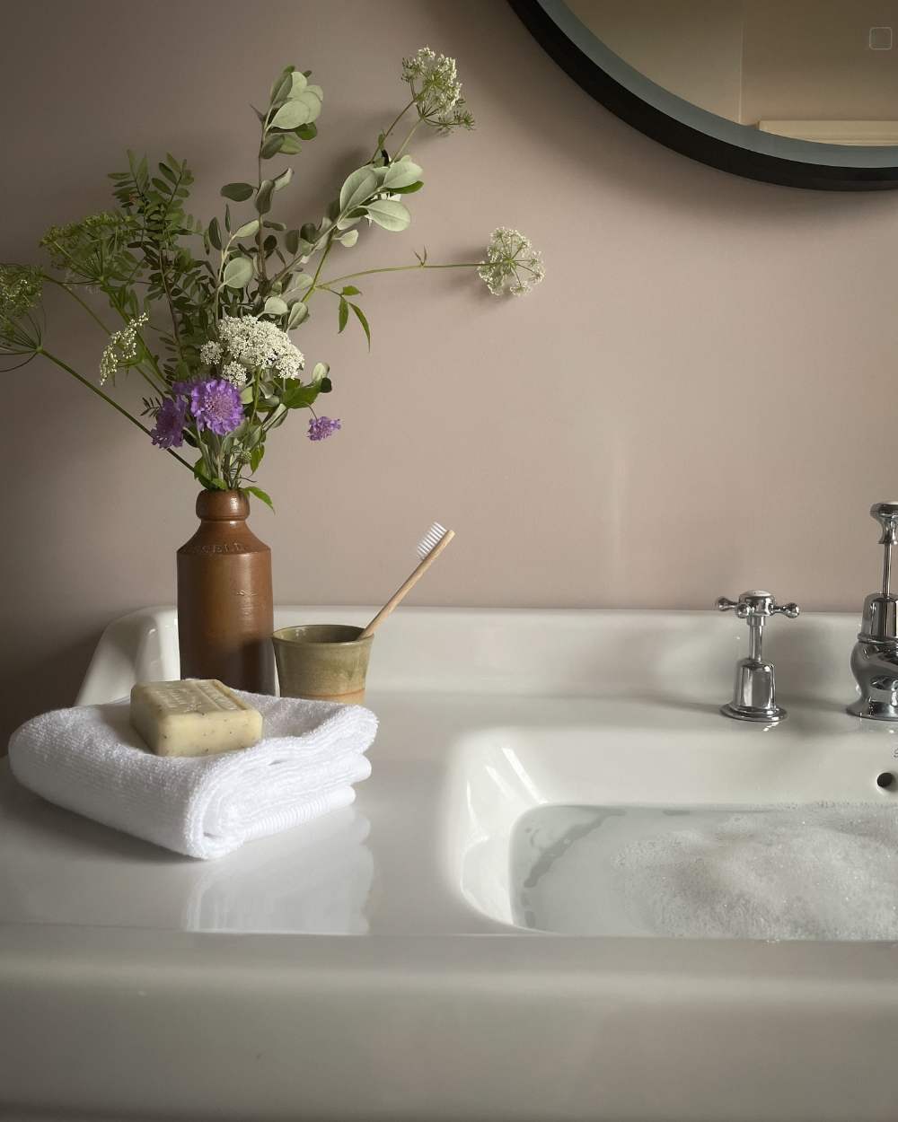 Carefully chosen items enhance the bathing experience, transforming it into a ritual of relaxation and rejuvenation from the Wild in the Wold An Ode To Calm Interior Collection featuring a soap and small earthenware vase with wild flowers