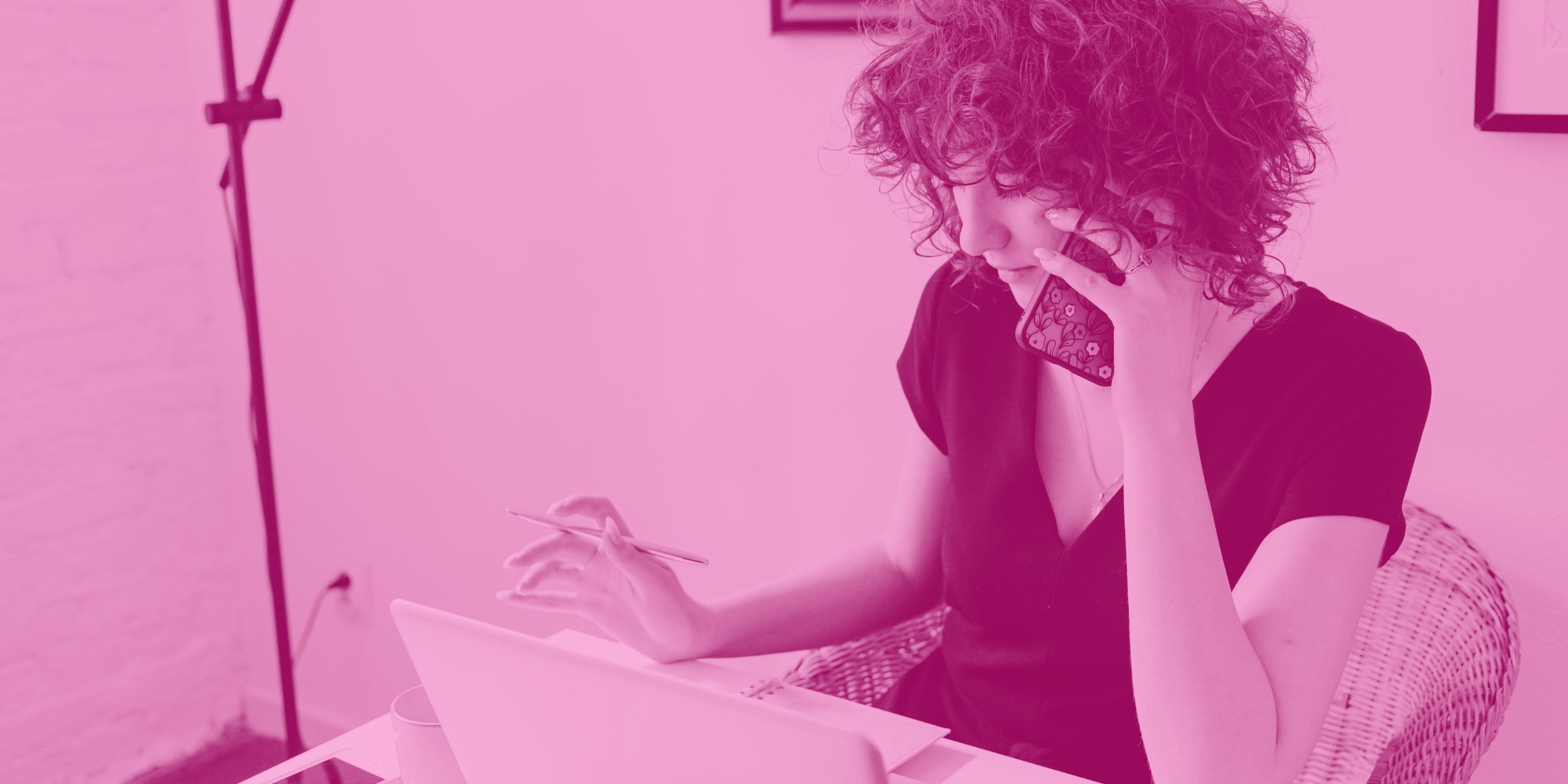 Woman on a phone talking with companies who want to advertise on PLEB magazine, with a pen in her hand sitting in an office with a pink overlay on the image