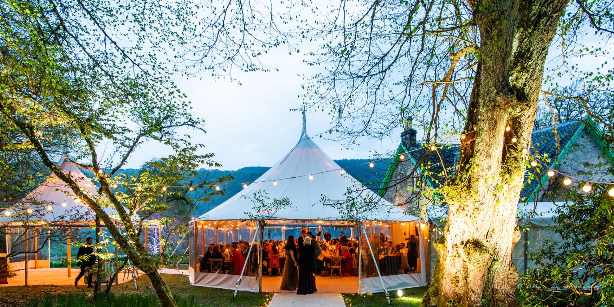 Wild Weddings Events by Sauveur, a wedding tent in the great outdoors with tables, fairy lights and trees surrounding it - Image credit Aurelien Langlais