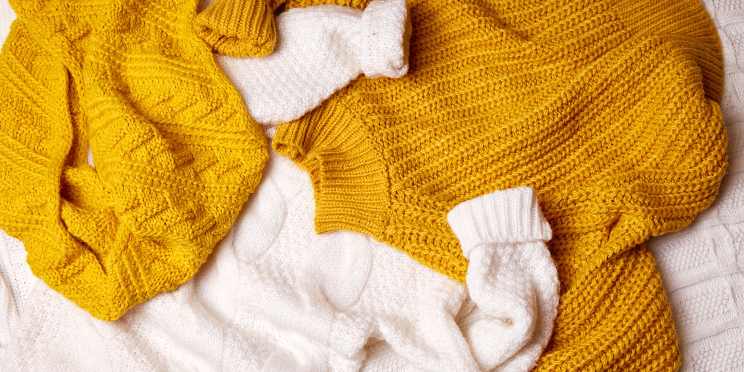 Caring for Cashmere yellow and white cashmere jumpers on a bed in a pile