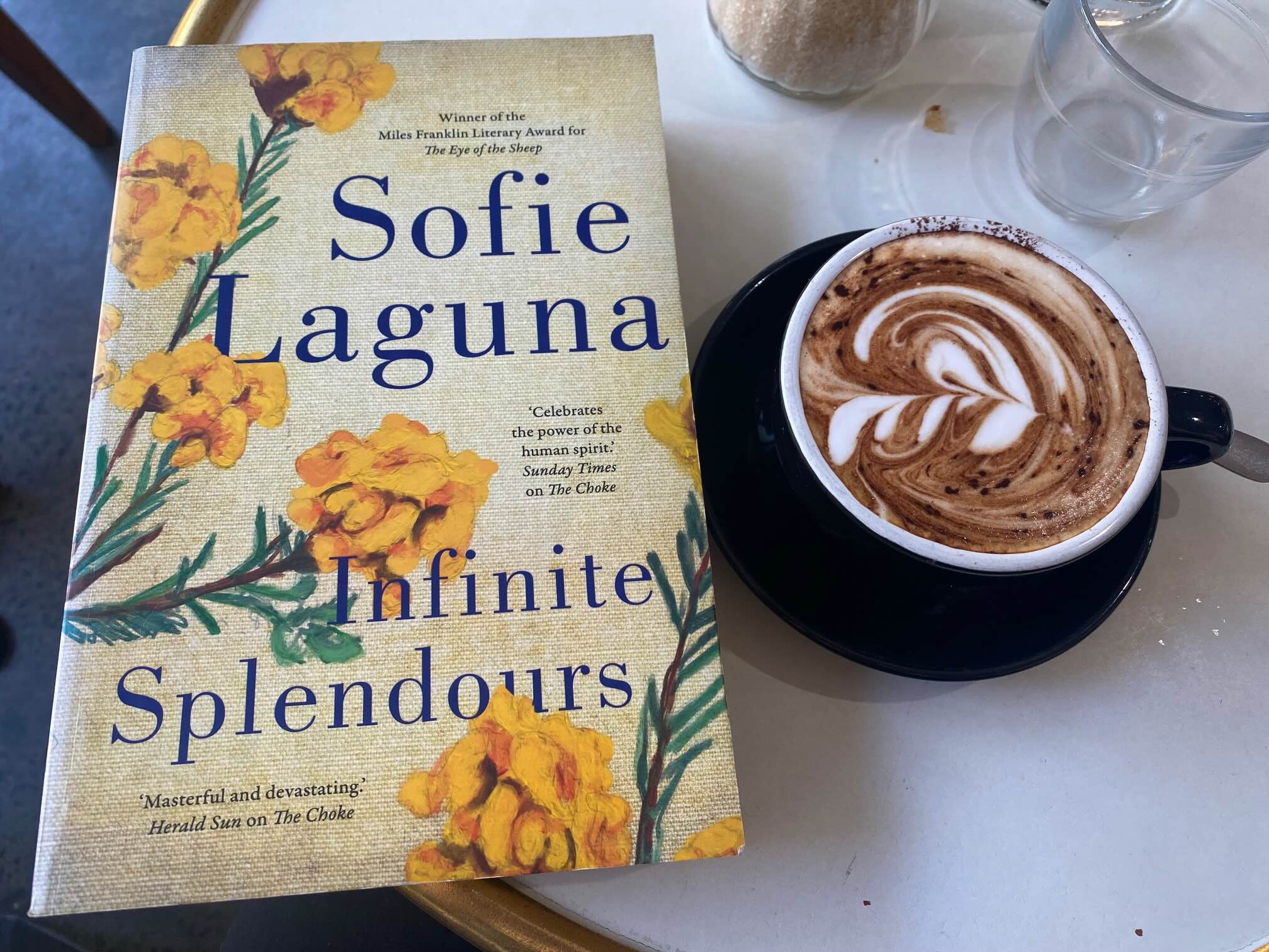 Infinite Splendours by Sofia Laguna book cover next to a cup of coffee