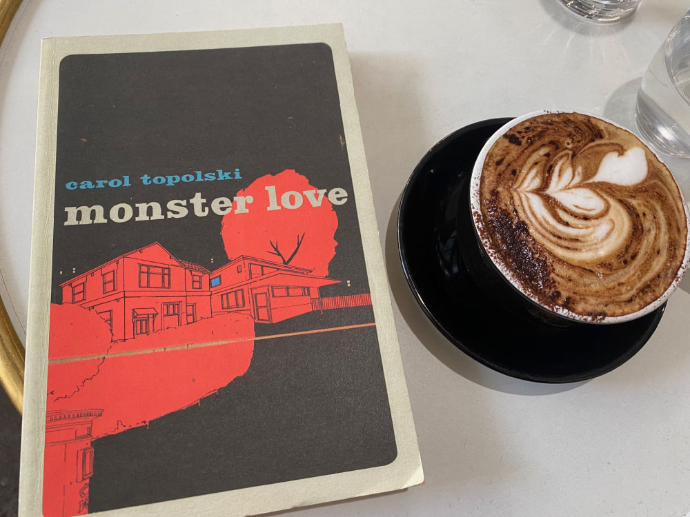 Monster Love by Carol Topolski book cover next to a cup of coffee on a table.