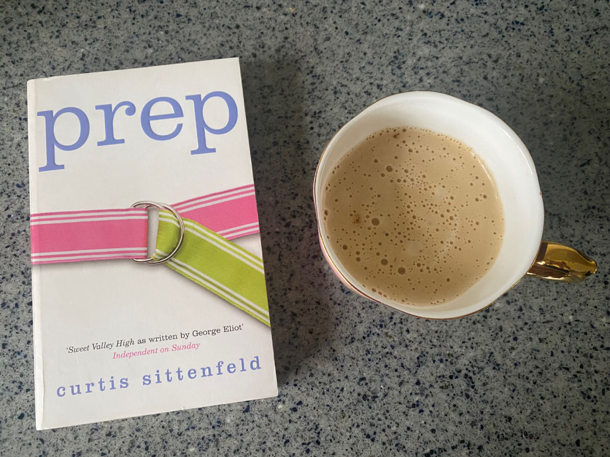 Prep by Curtis Sittenfeld Book Cover next to a coffee in a gold cup on a marble table.