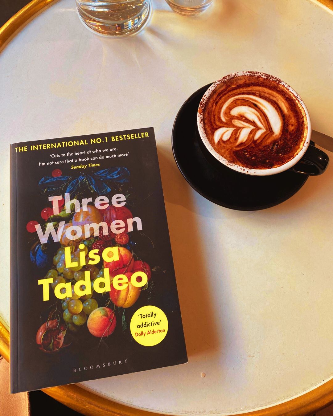 Three Women by Lisa Taddeo book cover on a table next to a cup of coffee