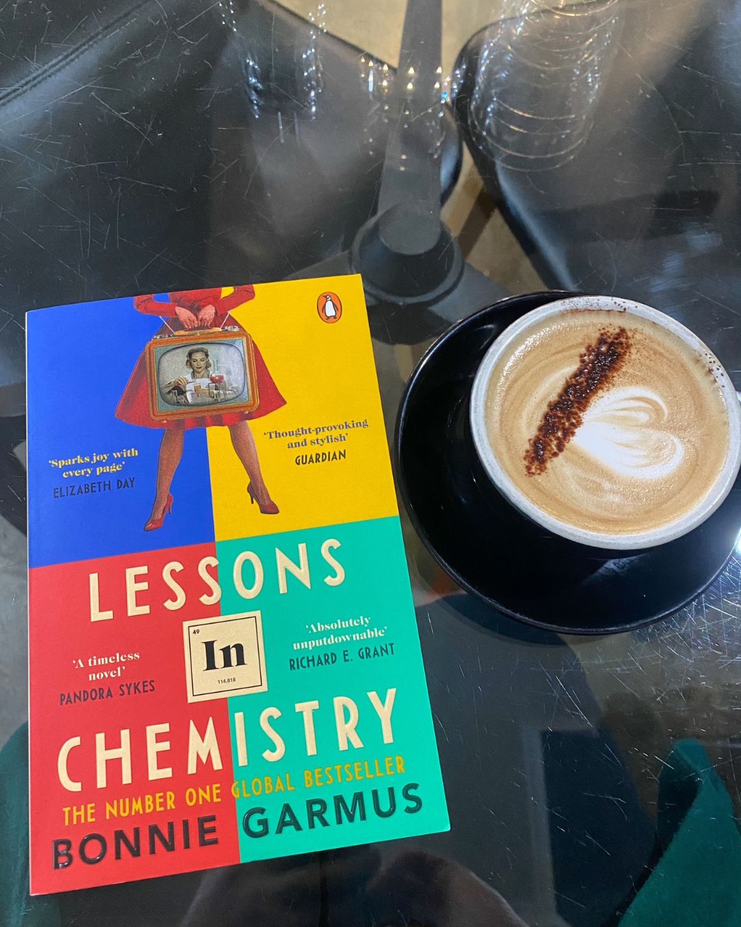 Lessons in Chemistry by Bonnie Garmus book cover on a coffee table next to a cup of coffee