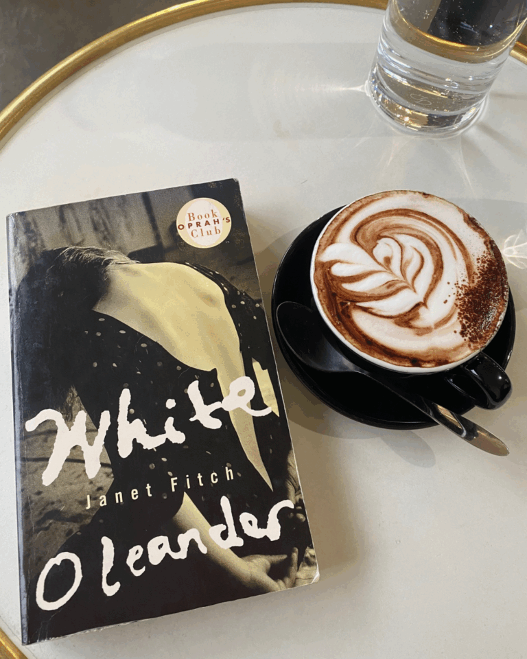 White Oleander by Janet Fitch book cover on a coffee table next to a cappuccino