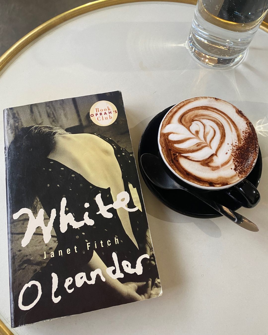 White Oleander by Janet Fitch book cover on a coffee table next to a cappuccino